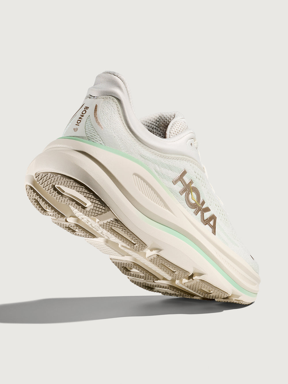 Chunky soled white Hoka running shoe with pastel green trim. 