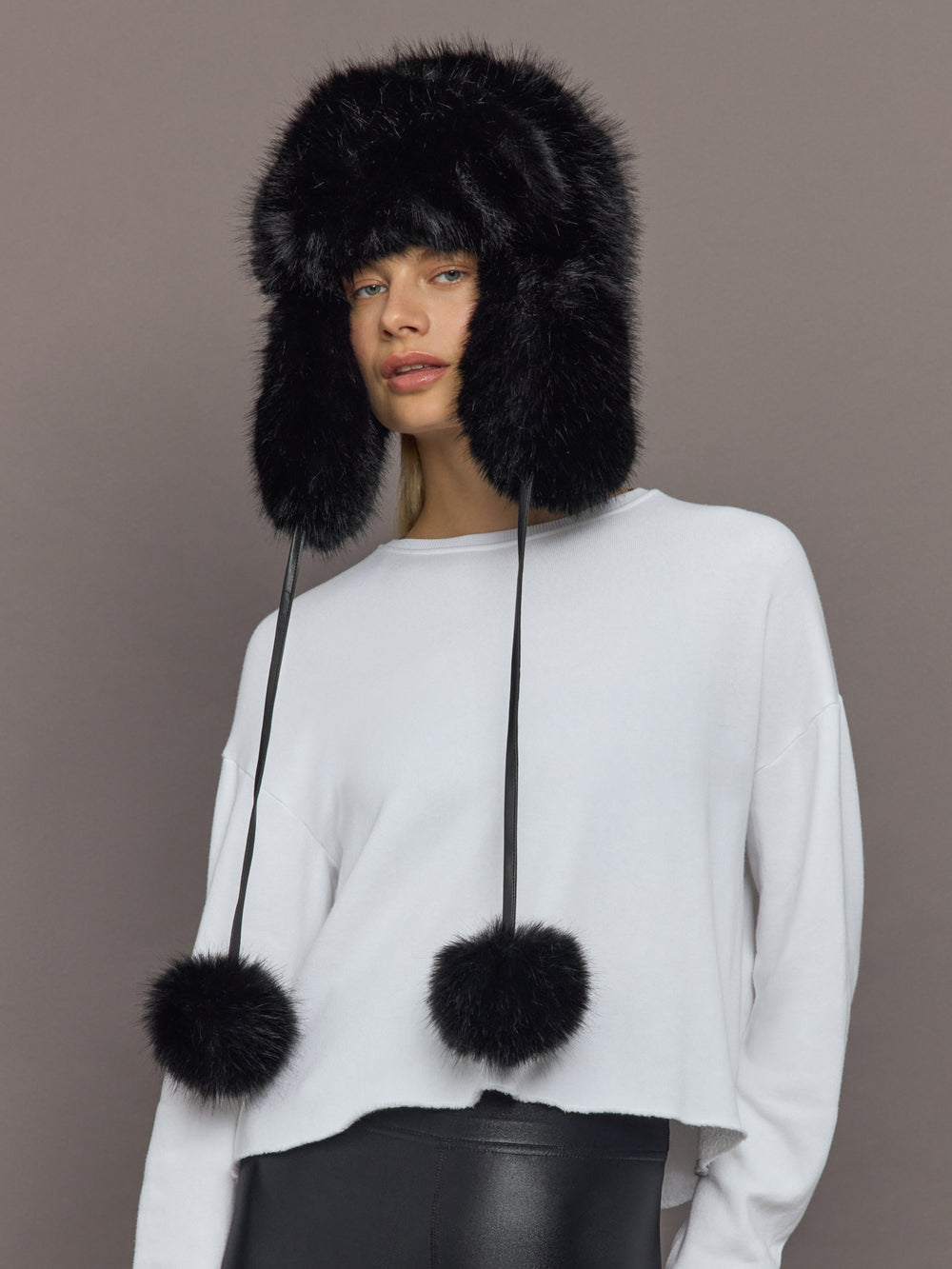 Model wearing Fox Trapper Hat in black faux fur, front view with pom-pom ties.