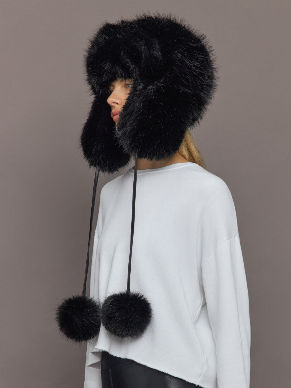 Side view of Fox Trapper Hat in black faux fur with long pom-pom ties.