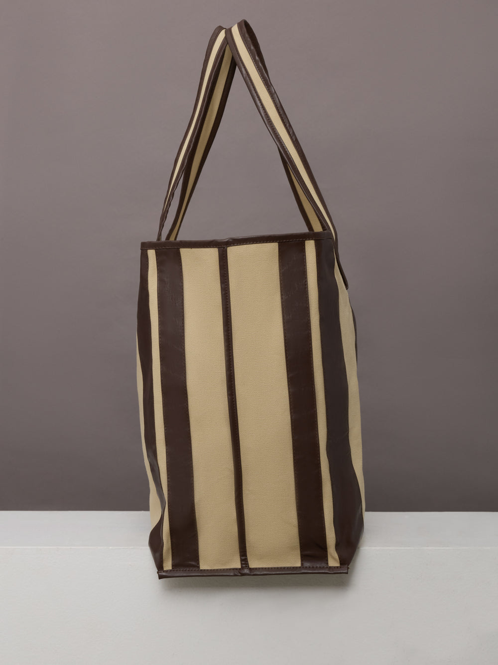 Beige canvas tote bag with black leather bindings, two straps, and an inner pocket.
