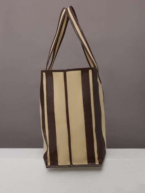 Beige canvas tote bag with black leather bindings, two straps, and an inner pocket.
