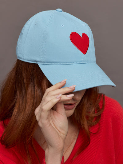 Model wears a baby blue baseball cap with a big red heart front and center. 