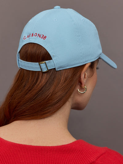 Model wears a baby blue baseball cap with a big red heart front and center. Back of hat says Carbon38 in red uppercase lettering. 