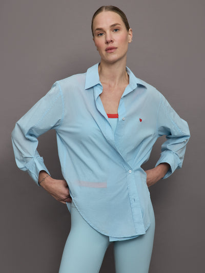 Model wears light blue button down shirt with tiny red heart over left side of chest.