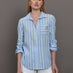 Model wears a striped blue and white buttondown long sleeve with single chest pocket. 