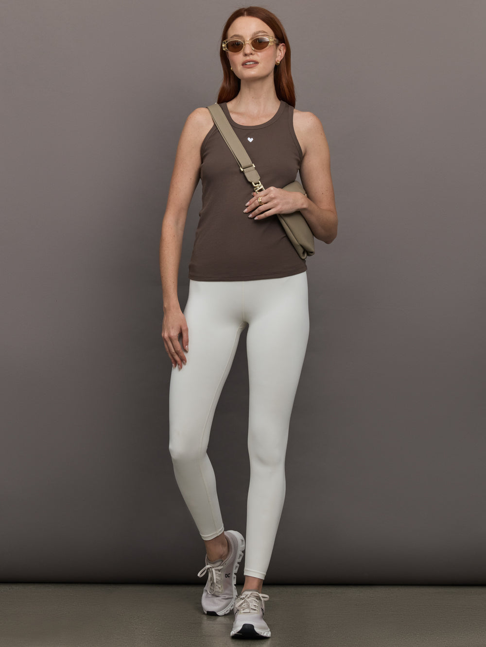 Model wears sleeveless tank top in a cocoa brown, featuring a scoop neckline and fitted silhouette and white heart in the upper center.