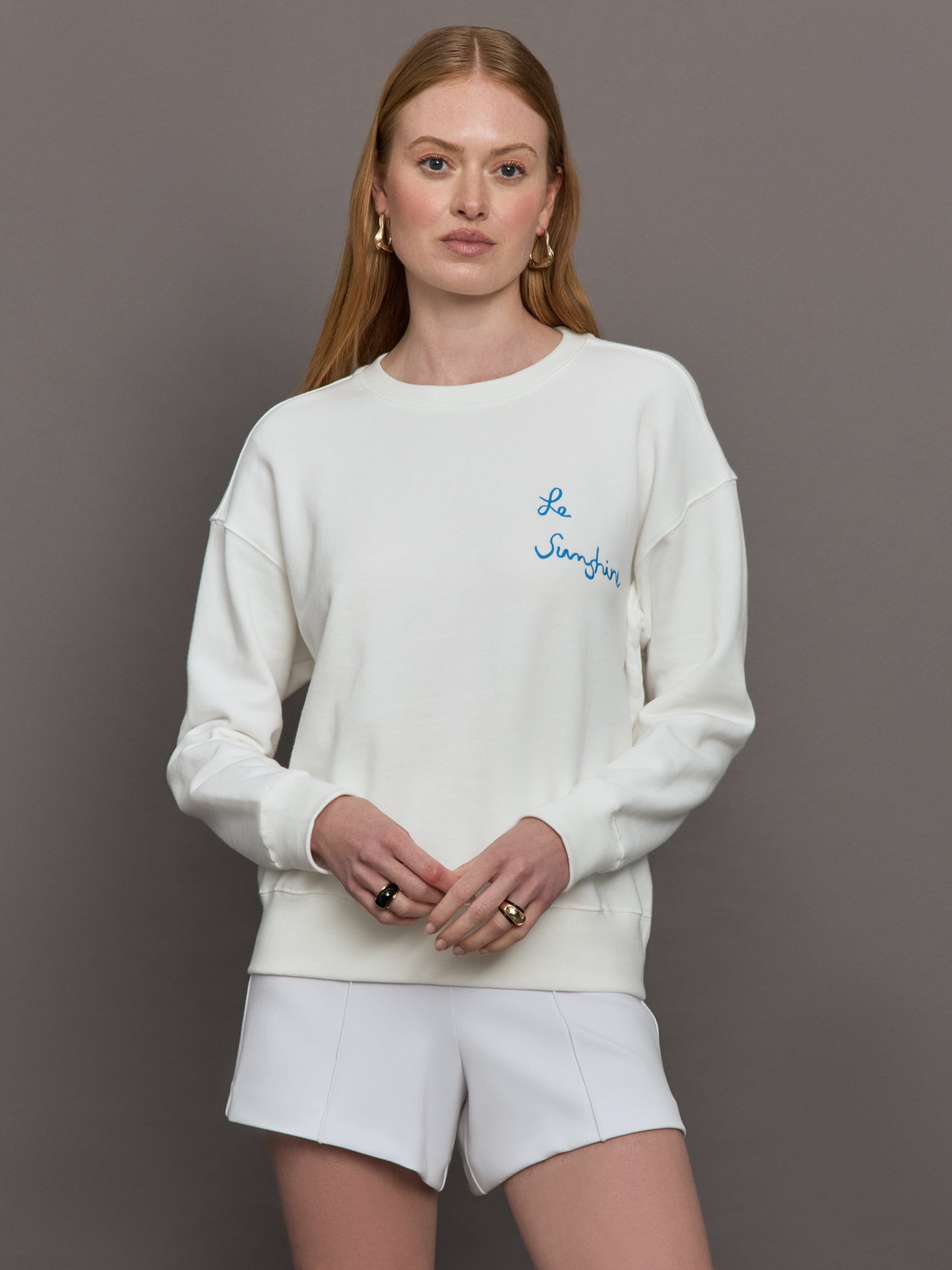 Model wears a white crewneck sweatshirt with script lettering "Le Sunshine" in blue on left side of chest.