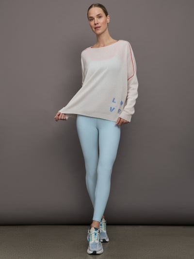 Model wears a white sweater with red seams along the biceps and blue block lettering on front bottom right that says LOVE. Back of sweater says in blue lettering "Love is all around you."