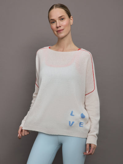 Model wears a white sweater with red seams along the biceps and blue block lettering on front bottom right that says LOVE. Back of sweater says in blue lettering "Love is all around you."