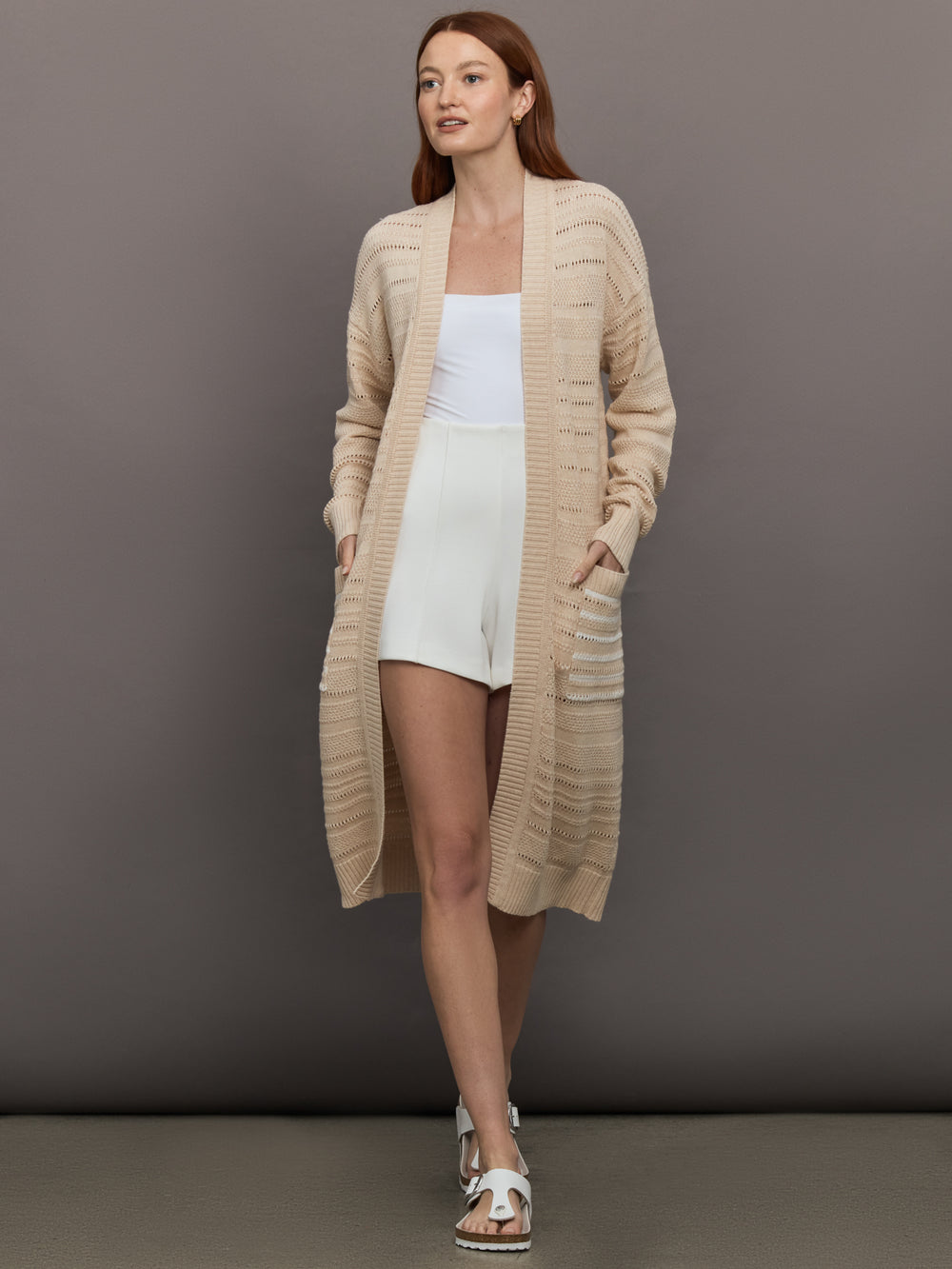 Model wears long, lightweight duster-style sweater in a natural beige tone.