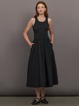 Model wears sleeveless black tank dress with a scoop neckline and lower waist drop.