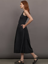 Model wears sleeveless black tank dress with a scoop neckline and lower waist drop.