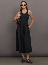 Model wears sleeveless black tank dress with a scoop neckline and lower waist drop.