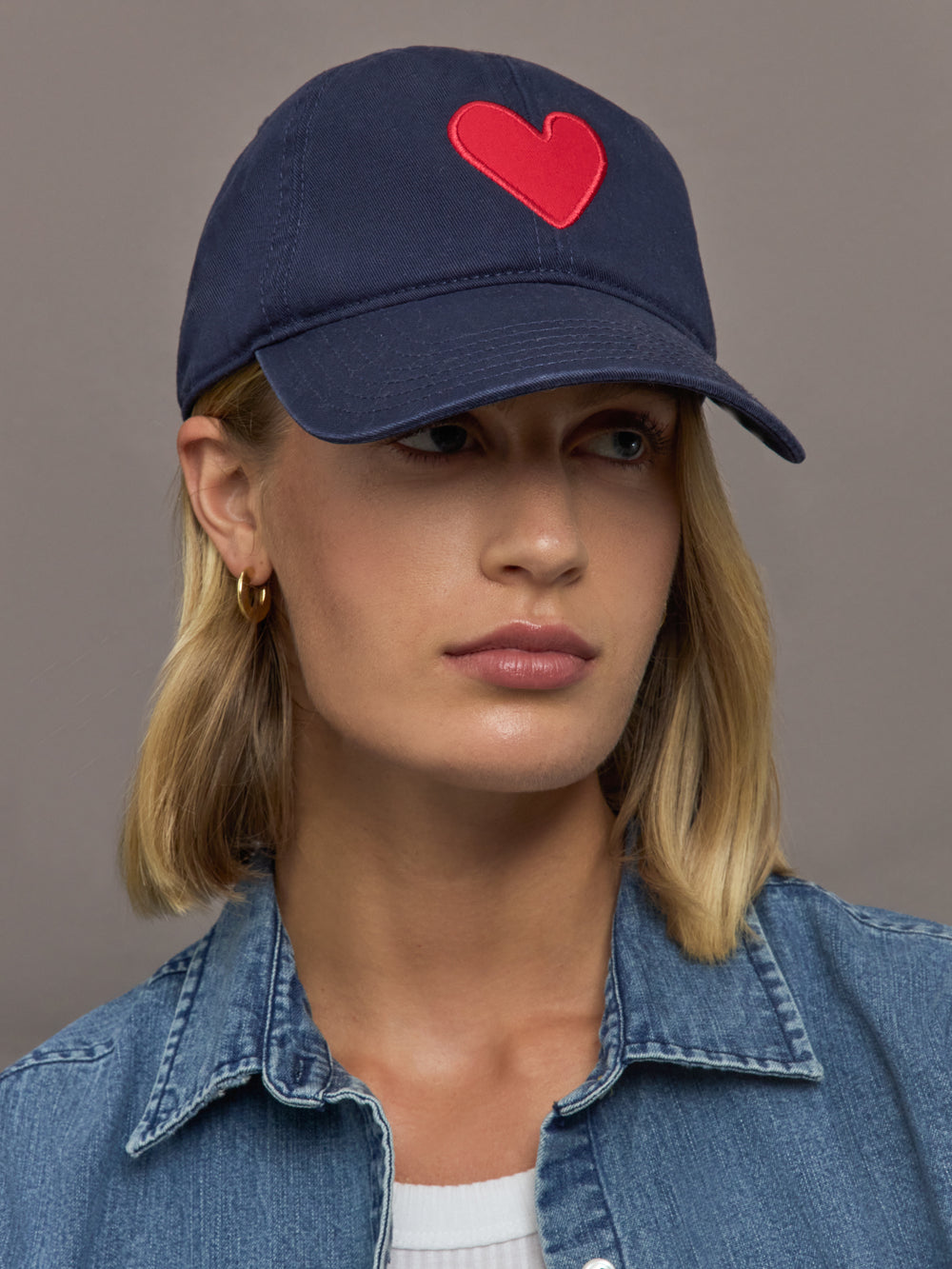 Person wearing a navy cap with a red heart on a plain background