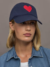Person wearing a navy cap with a red heart on a plain background