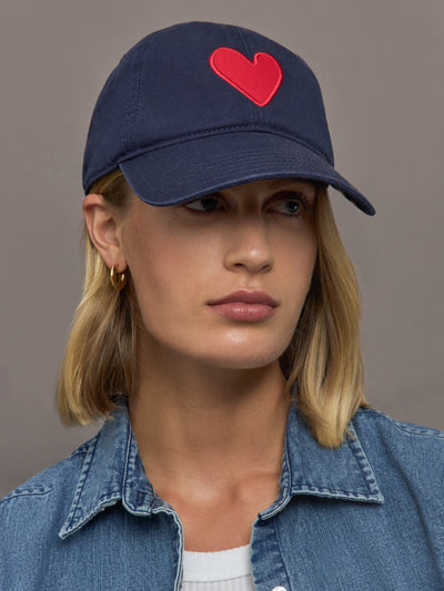 Person wearing a navy cap with a red heart on a plain background