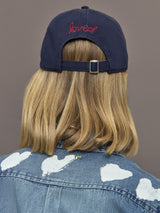 Person wearing a navy cap with 'loved' embroidered on it, facing away from the camera.