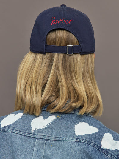 Person wearing a navy cap with 'loved' embroidered on it, facing away from the camera.