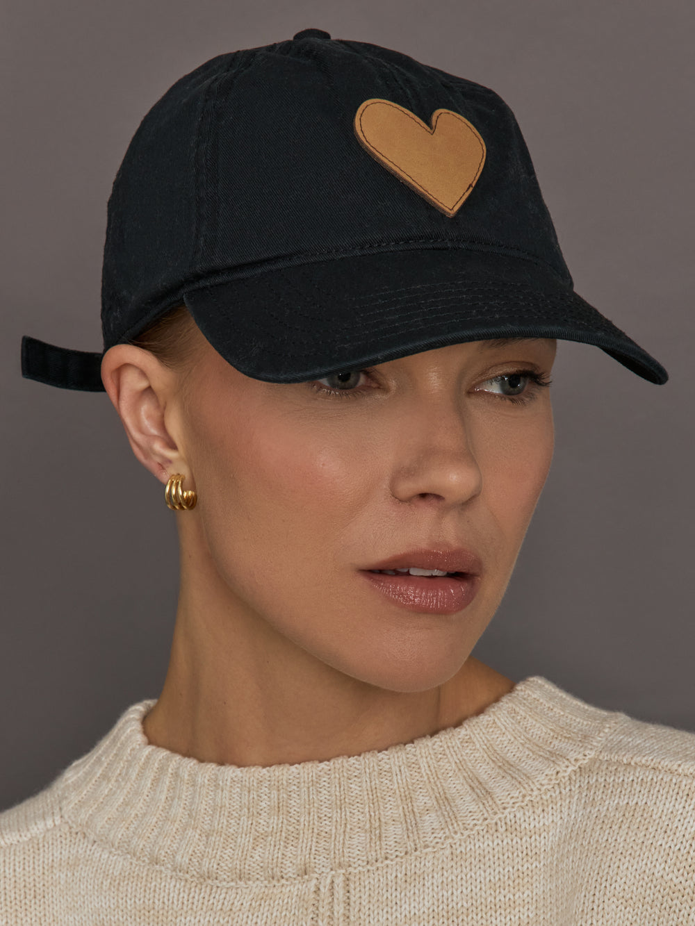 Person wearing a black cap with a gold embroidered heart.