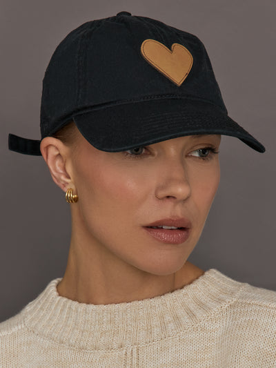 Person wearing a black cap with a gold embroidered heart.