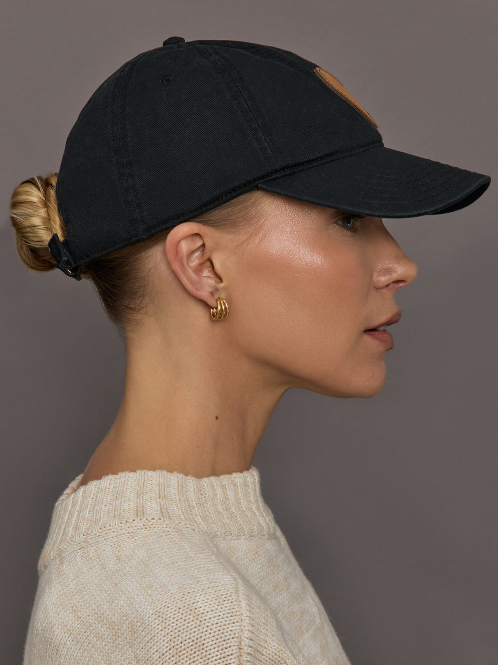 Woman wearing a black baseball cap with a gold embroidered heart on the front
