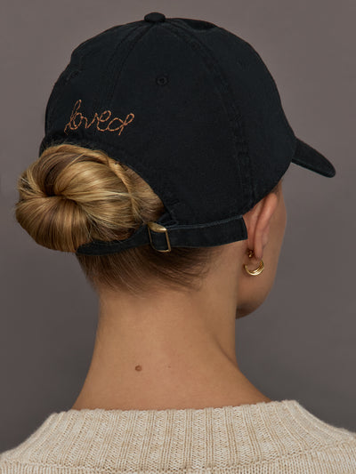 Person wearing a black cap with 'loved' embroidered on the back.