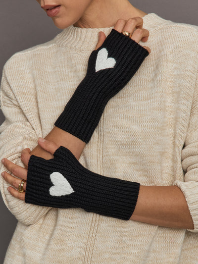 Black fingerless gloves with white heart designs worn by a person in a beige sweater.