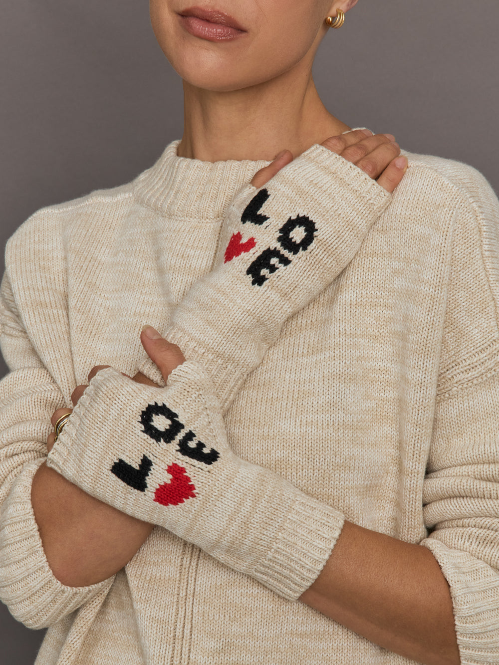 Person wearing a beige sweater with beige gloves that say "LOVE" with a red heart detail.
