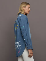 Woman wearing a blue denim jacket with colorful paint splashes and text on a gray background