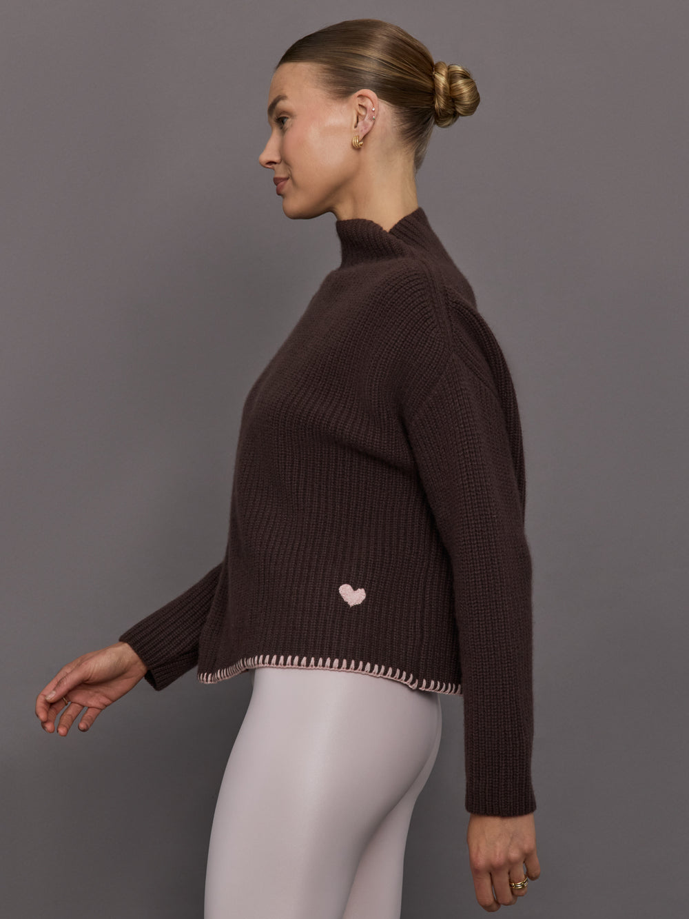 Woman wearing a brown ribbed sweater with a pink heart detail on the bottom 