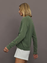 Woman wearing a green sweater and white shorts against a gray background