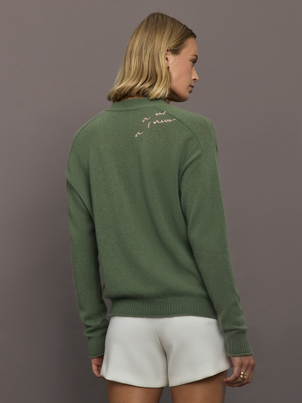 Woman wearing a green sweater with text on the back against a gray background