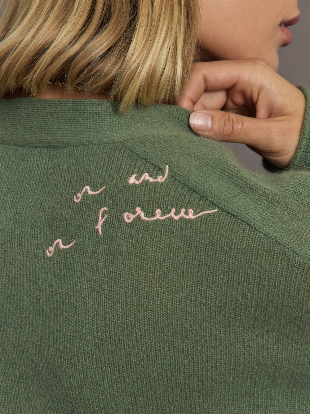 Green sweater with pink embroidered text on a neutral background