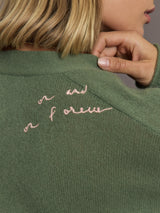 Green sweater with pink embroidered text on a neutral background