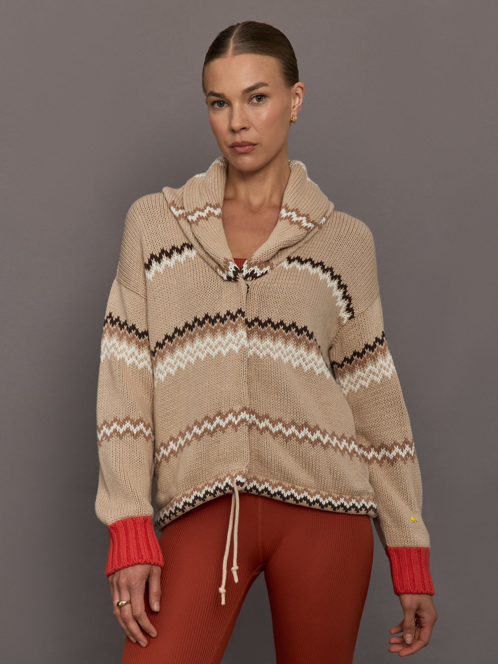 Beige knitted cardigan with patterned design and red cuffs on a neutral background
