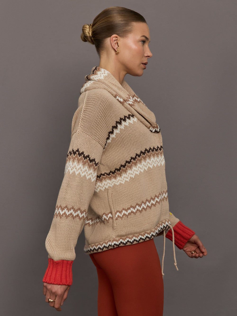 Beige knitted cardigan with patterned design and red cuffs on a neutral background
