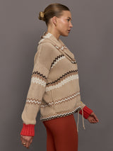 Beige knitted cardigan with patterned design and red cuffs on a neutral background