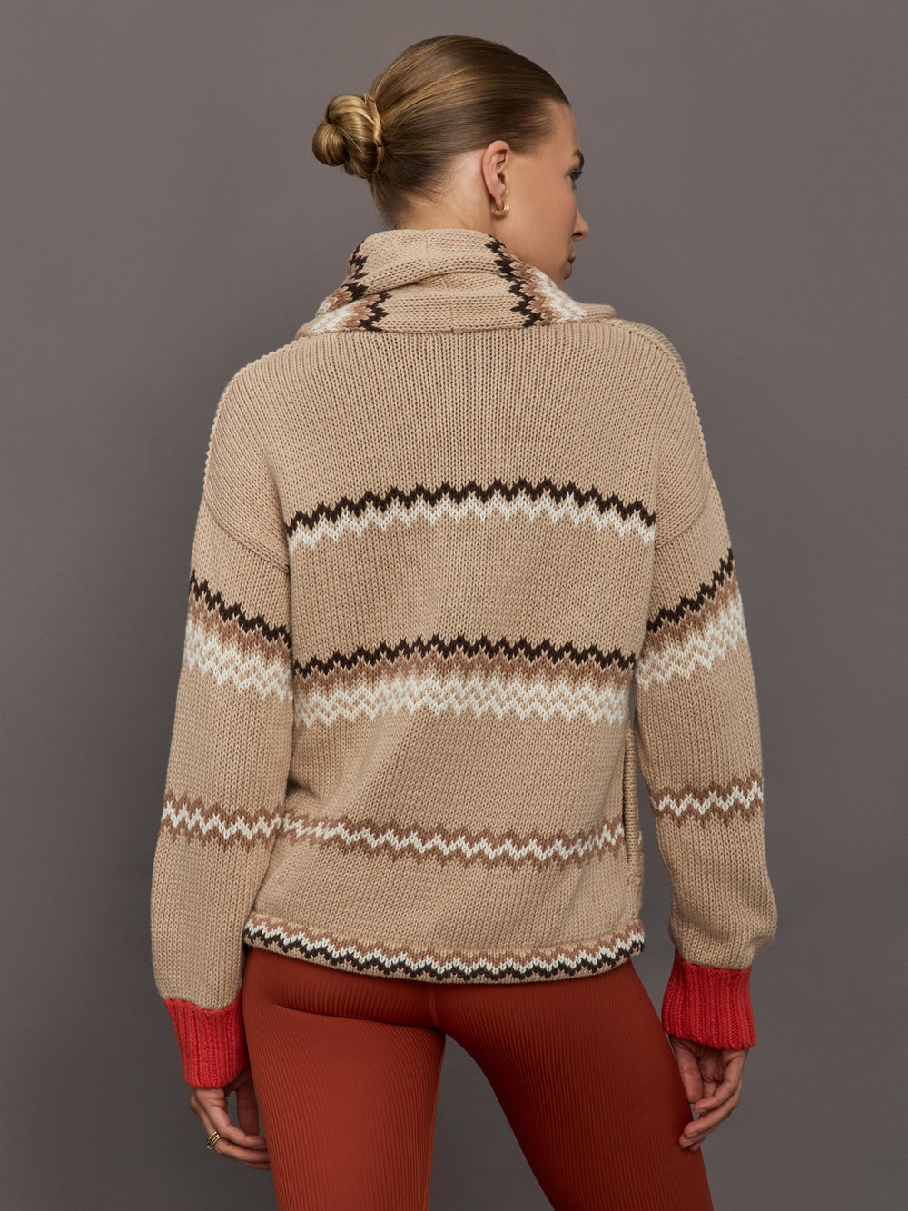 Beige knitted cardigan with patterned design and red cuffs on a neutral background