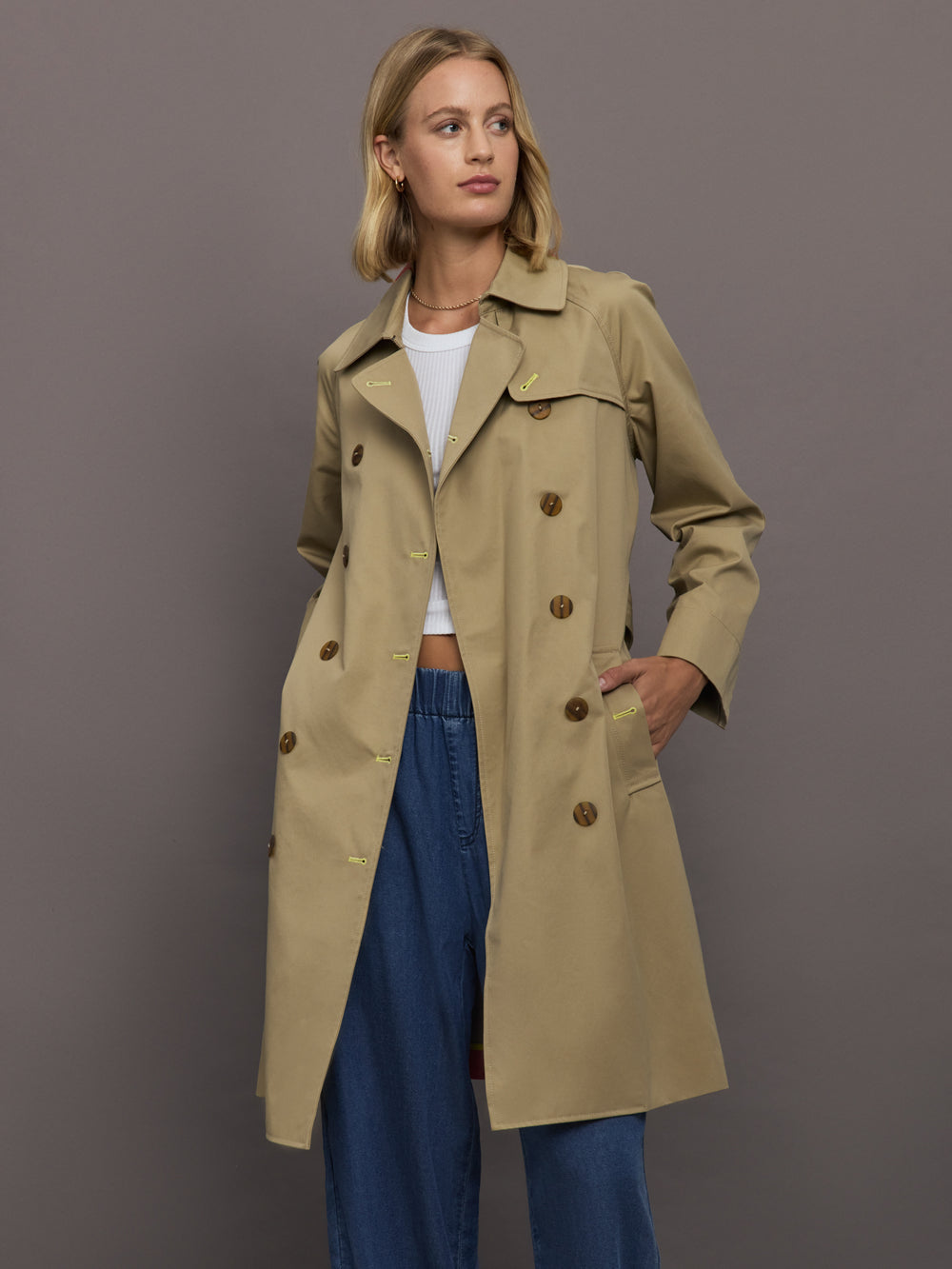 Woman wearing a beige trench coat against a gray background