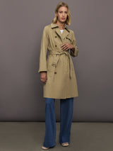 Woman wearing a beige trench coat and blue jeans against a gray background