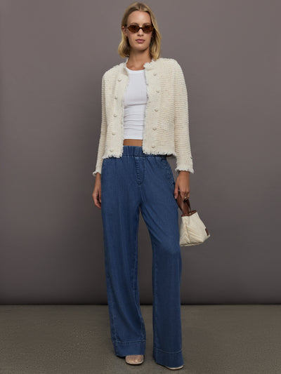 Woman wearing a white cardigan, white top, blue pants, and sunglasses against a gray background