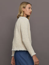 Woman wearing a textured beige sweater and blue jeans against a gray background