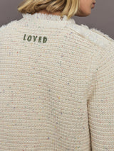 Back view of a textured beige sweater with 'LOVED' embroidered on it against a neutral background.