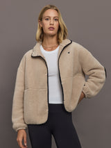 Model wears a camel colored fleece jacket with tiny black embroidered heart on chest and elbows. 