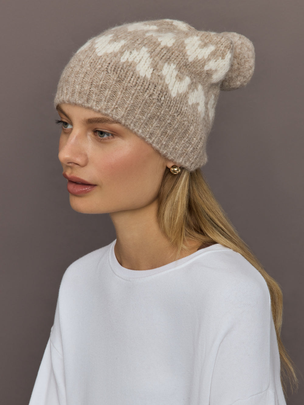 Model wearing camel alpaca-merino beanie with ivory hearts, front angle view.