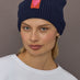 Model wearing indigo blue cotton-cashmere beanie with pink heart patch, front view.