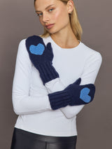 Model wearing indigo blue knit mittens with heart patches, front view with crossed arms.
