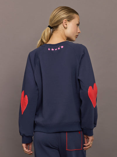 Model wearing indigo blue heart patch sweatshirt, side view showing red elbow patch.