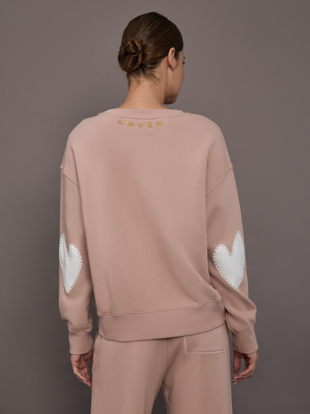 Model is wearing Ex-Boyfriend fleece relaxed crewneck sweatshirt in mauve, back view with Loved artwork.