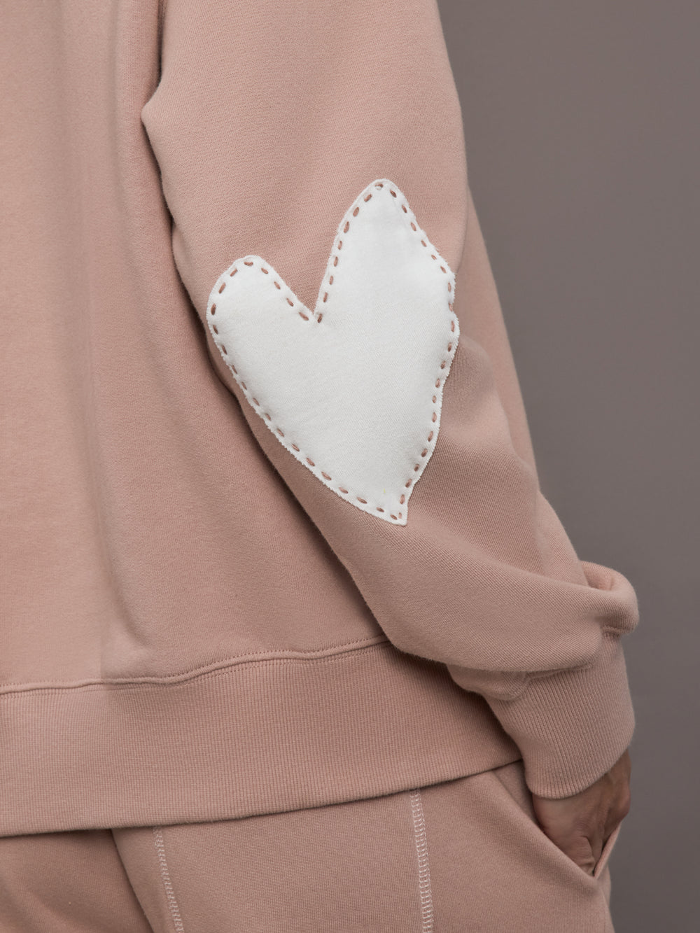 Model is wearing Ex-Boyfriend fleece relaxed crewneck sweatshirt in mauve, close-up of Imperfect Heart patch.